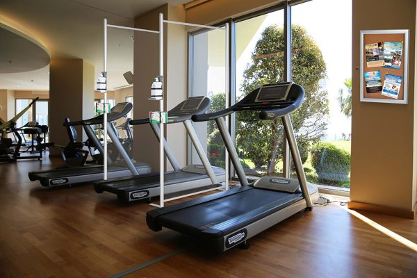 Treadmills facing a window with clear wall separators between them with a locking show board with fliers in it on the wall