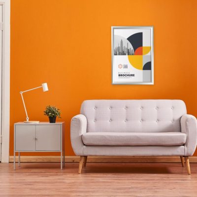 Poster hanging in a snap poster frame with a mitered corner on an orange wall above a cream couch with a side table next to it