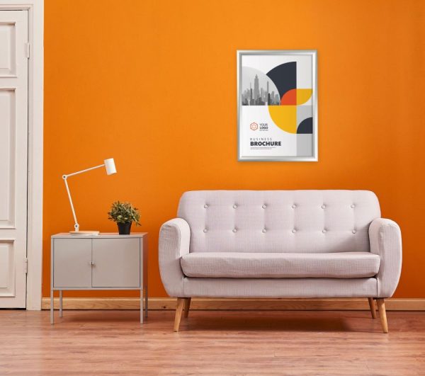 Poster hanging in a snap poster frame with a mitered corner on an orange wall above a cream couch with a side table next to it