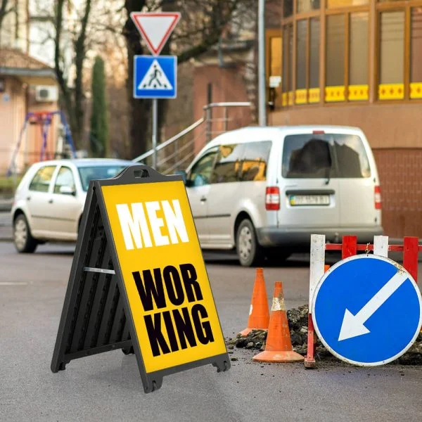 Men Working sign on a black A-Frame SignPro Sidewalk sign in the street next to a man hole that workers are fixing