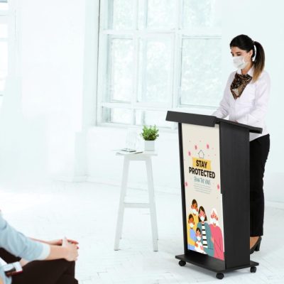 woman giving a speech to a very attentive crowd behind a wooden podium