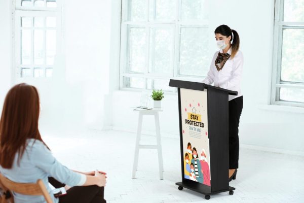 woman giving a speech to a very attentive crowd behind a wooden podium