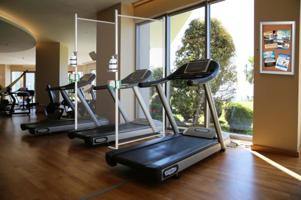 Clear wall Separators in with glove box holders and hand sanitizer holders in between treadmills at a gym