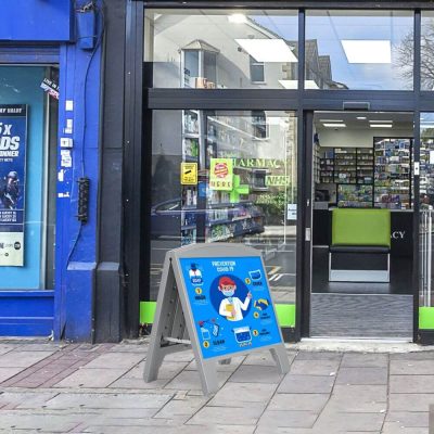 Sandwich Board A-Frame outside of a pharmacy with a poster of COVID precautions on it