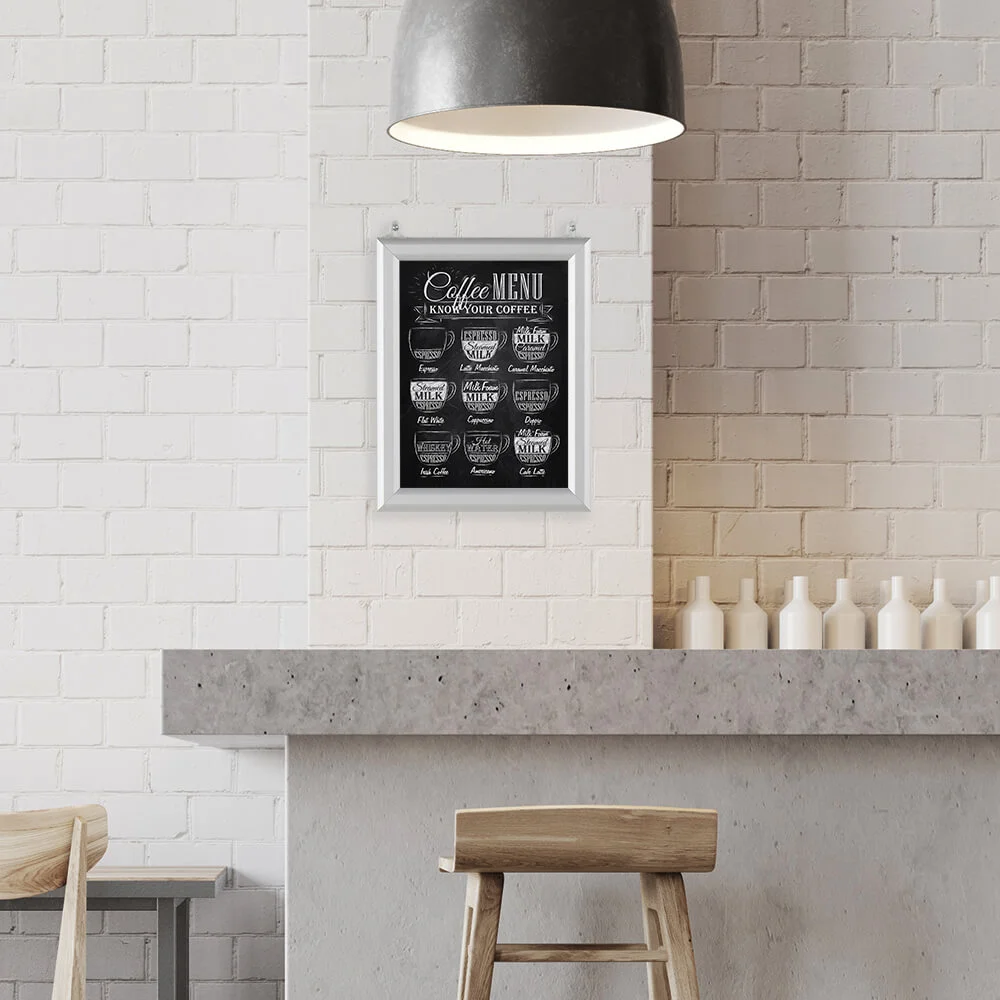 8-5x11-slide-in-frame-1-inch-silver-mitered-profile-double-sided-2-pack A coffee menu hanging in a Slide in Frame on a white brick wall in a minimalist style coffee shop