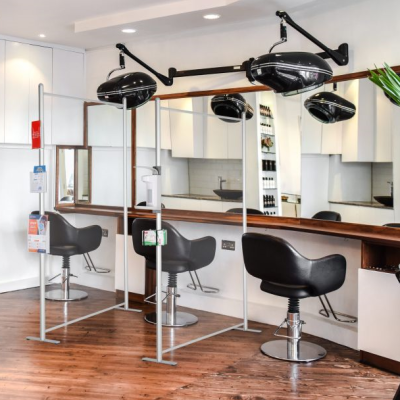 Clear wall panels with hand sanitizer dispenser connected to the edge separating salon chairs