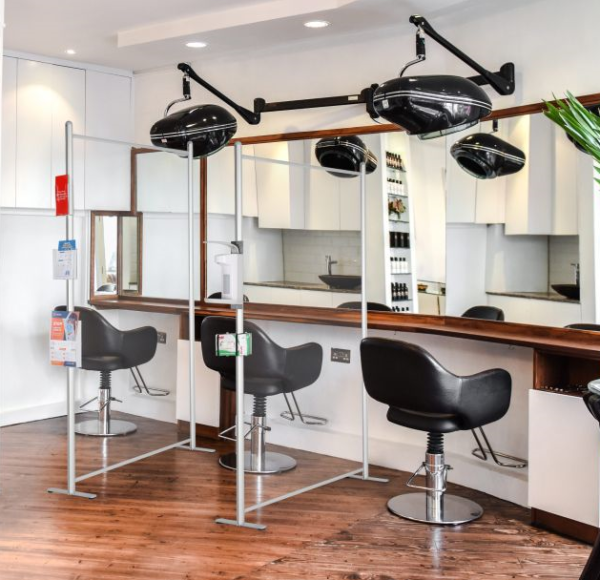 Clear wall panels with hand sanitizer dispenser connected to the edge separating salon chairs