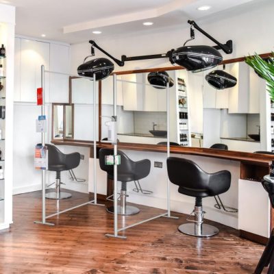 Clear wall panels with hand sanitizer dispenser connected to the edge separating salon chairs