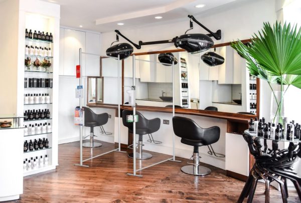 Clear wall panels with hand sanitizer dispenser connected to the edge separating salon chairs