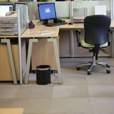 an office cubical with a green rolling chair and black open top waste basket