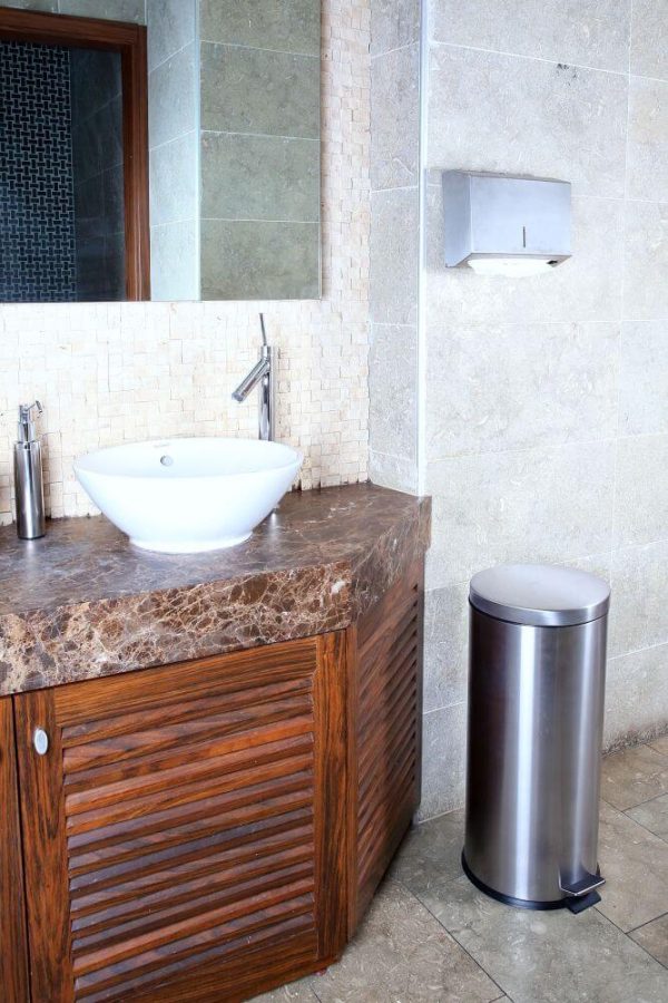 Bathroom Sink with a paper towel holder hanging on the wall above a silver step on trash can